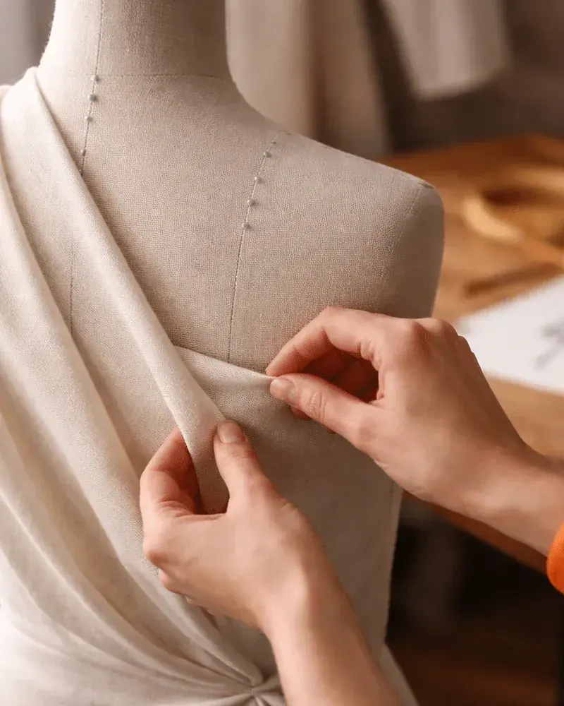 Manos colocando una tela sobre un maniquí en el taller